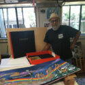 man with artists' book open to his painting